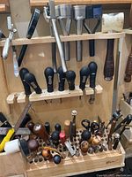 Wooden tool rack holding metal punches and chisels with black plastic handles plus bottom row of wooden-handled tools