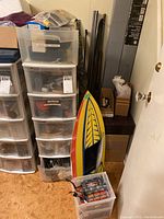 Two clear plastic drawer towers, a small bin containing battery pack and batteries, red-yellow model boat hull leaning