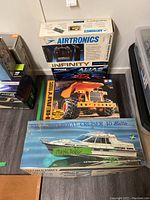 Photo of Storbro Royal Cruiser 40 Baltic RC boat kit, Tamiya Heavy Dump Truck box, and Airtronics Infinity 6GX2 controller box grouped on floor.
