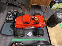 Red remote control monster truck showing body, wheels, and part of accessories including controllers and tire.
