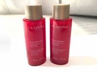 Two new 100 ml Clarins Multi-Intensive Super Restorative Treatment Essence bottles, red with gold caps, showing front labels.