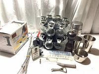 Photo of lot showing spice rack with 16 glass jars, Peugeot pepper mill, measuring cups, stainless steel mugs, cruet bottle, kitchen whisk, bottle opener, plastic syringe, and other kitchen items.