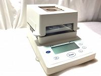 Front angled view of the moisture analyser showing the digital display, control buttons, and top mesh heating chamber.