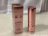 Lipstick in tube with box standing upright on fabric background.