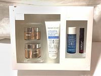 Full set showing two gold jars for creams, white tube for cleansing gel, blue bottle and dark tube in separate compartment.