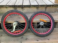 Pair of kids bike tires with wheelsets placed side by side on wooden steps. Tires mounted on red metal rims with spokes and reflectors.