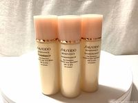 Three bottles of Shiseido Benefiance Wrinkle Resist 24 Day Emulsion 30ml each shown upright on a fabric surface with light pink caps and gold band.