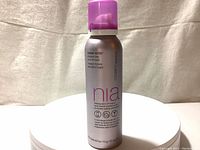 Full frontal view of StriVectin Nia-114 Sunday Detox whipped clay peel-off mask in metallic bottle with purple spray pump on top, standing on white surface against fabric background.