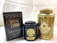 Three vintage tin cans: a tall gold Windsor Castle tea tin with dent, a smaller black Mariage Freres Marco Polo tea tin, and a black NABOB Special Edition Kenya Ibonia Estate coffee tin.