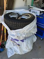 Four silver alloy wheels with mounted black Winter i*Cept snow tires stacked in plastic storage bags on garage floor.