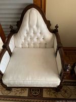 Close-up front view of one chair showing tufted off-white fabric upholstery, wood framing with decorative finials at top corners.