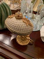 Close-up image of a detailed Faberge egg replica showing white lattice work, gold floral accents, and a decorative gold stand.