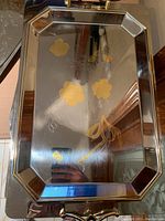 Photo of rectangular stainless steel serving tray with gold handles, gold trim, and embossed floral and ribbon etching on surface.