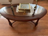 Full top view of oval mahogany coffee table with glass insert and decorative objects on top, showing carved edges and legs.