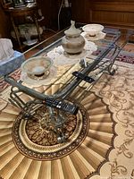 Top view of the rectangular glass coffee table showing the metal frame with silver and gold tones and curved leg details positioned on a patterned rug.