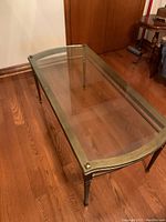 Curved glass top coffee table with metallic bronze frame and tapered legs on wood floor.