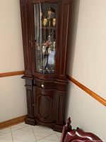 Front angled view of mahogany corner display cabinet showing curved glass door, wooden frame, knob, interior shelves and lower door.