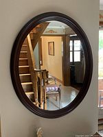 Oval mirror hanging on a wall reflecting a staircase and hallway, showing the entire frame and mirror surface.