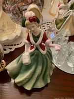 Porcelain figurine showing a Victorian woman in a green dress with red and white jacket and hair bow, holding a muff.