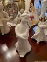 Close-up of white matte porcelain sister figurine with arms crossed, highlighting form and detail.