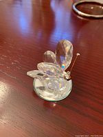 Clear faceted crystal butterfly with silver wire antennae on a wooden surface with an out-of-focus ring in background