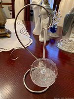 Clear glass Christmas ball ornament with white snowflake detail and embedded Swarovski crystal on metal display stand with white hanging ribbon.