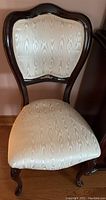 Front view of an upholstered wooden accent chair showing cream patterned fabric and curved wooden legs.