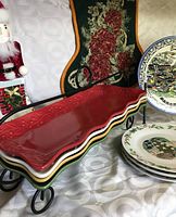 Photo of red ceramic serving tray on black metal stand with surrounding Christmas plates and decorations