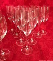 Close-up showing 10 champagne/prosecco flutes with slender tall shapes and 2 white wine glasses in front of them