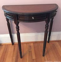 Photo of front view of demi lune hall table, showing dark wood legs and leather-like curved top.