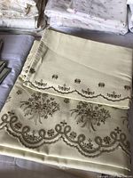 Close-up of cream-colored double bed sheet with detailed brown embroidered floral lace and scalloped edges.