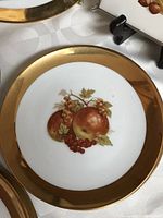 Close-up of a porcelain plate featuring a fruit motif with apples, red currants, and gold rim