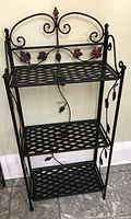 Full view of the mini bakers rack showing all three shelves, grapevine decorative metalwork, and foldable design.