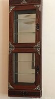 Front view of the entire wooden display case showing glass doors with metal decorative corners, glass shelves inside, and mirrored back panel.