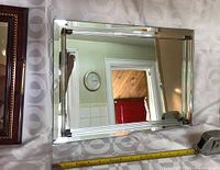 Beveled mirror tray with clear glass rod accents and silver-tone metal ends showing reflective surface and partial measuring tape beneath to indicate size.