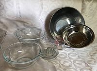 Photo showing entire kitchenware set with four glass Pyrex bowls, two stainless steel bowls, two measuring cups, and a glass juicer arranged on patterned fabric.