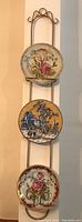 Full view of gold-colored metal plate hanger holding three decorative plates mounted vertically on wall.