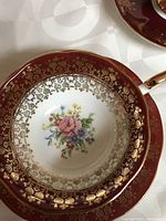 Close-up of deep cranberry red saucer showing detailed gold filigree and floral pattern
