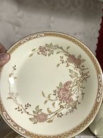 Close-up of dinner plate showing cream base with pink floral pattern and gold beige border.