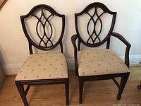 Pair of dining chairs shown with one armchair and one side chair, showcase seat upholstery and carved back designs.