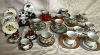 Full collection of espresso cups, green tea cups, and decorative miniatures arranged on tablecloth.