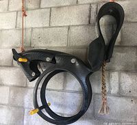 Close-up photo of the black horse-shaped tree swing made from recycled tires showing detailed horse face, yellow handles and foot rests, and braided rope tail.