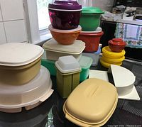 Overview of all Tupperware items arranged on a table showing different colors and sizes including the manual chopper, multiple containers, bowls, and the divided serving bowl.