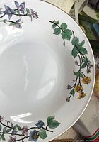 Close-up of soup/salad bowl showing cream-colored base with brown vines, green leaves, and yellow and purple flowers around the rim.