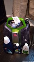 Photo of Bissell Little Green ProHeat steam cleaner with three bottles of accompanying cleaning solutions.