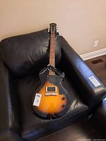 Full body view of sunburst Epiphone Junior guitar on black chair, shows single humbucker pickup, controls and included cable.