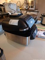 View of closed Ninja Foodi grill showing black and stainless steel body on counter with digital control panel.