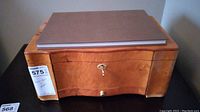 Closed polished wooden humidor box with lock and brass key inserted, plain top with book on it.
