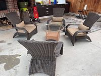 Overhead view of four brown resin wicker armchairs arranged around a glass-top wicker side table showing seat cushions and bolsters.