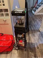 Overall view of black Nostalgia popcorn cart on wheels with kettle and lower shelf